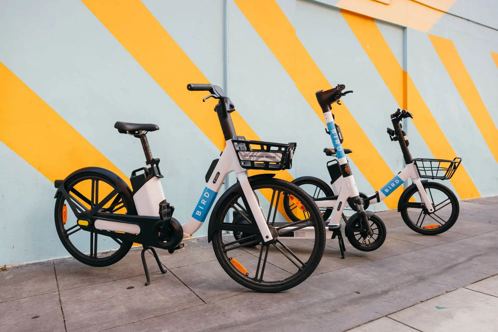 Bird e-bikes parked in front of a colorful yellow and teal mural